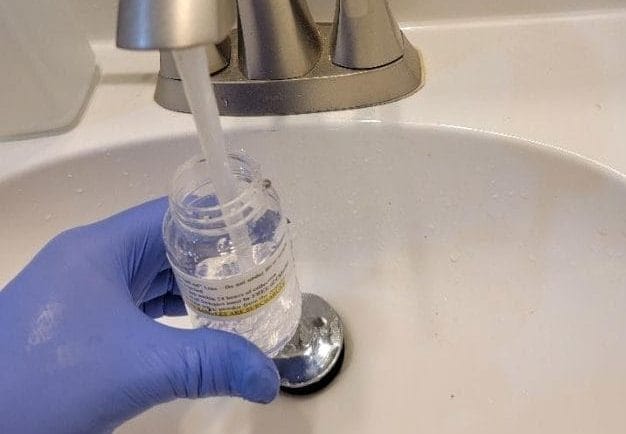 Gloved hand filling a vial with tap water at a sink
